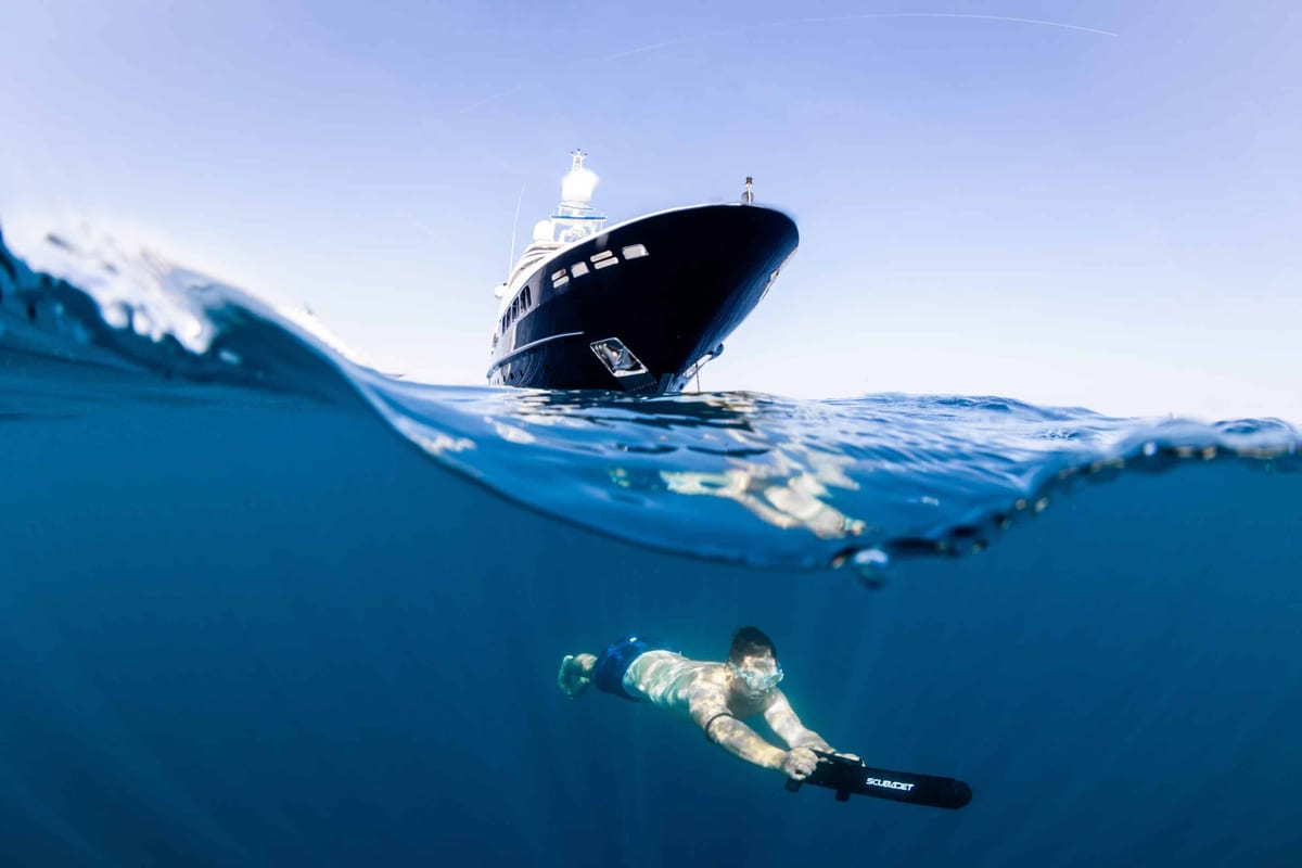 Split-level shot of a superyacht at anchor with a swimmer on an underwater scooter